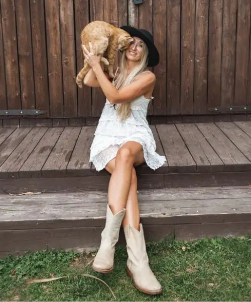 Woman in white dress and cowboy boots hugging a dog